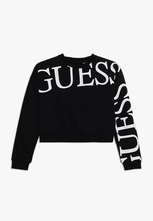 Sort cropped sweatshirt med lange ærmer med stor hvid "GUESS" tekst henover brystet og ned ad det ene ærme.