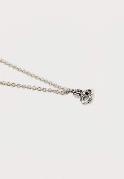 Collier chaîne en argent avec un petit pendentif en forme de hibou, orné d'yeux en pierre noire et de détails décoratifs.