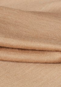 Tissu beige clair et doux avec une texture côtelée fine, soigneusement plié pour montrer le tissage lisse et les variations subtiles de couleur.