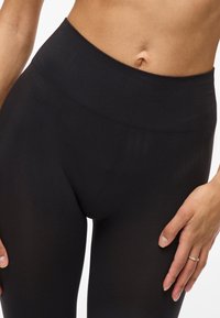 Leggings noirs taille haute en tissu extensible, avec une texture lisse et une large ceinture côtelée pour le confort.