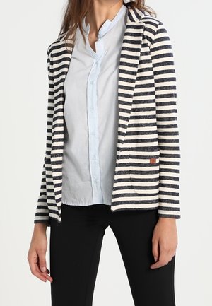 Blazer rayé en bleu marine et crème, avec une coupe décontractée, une ouverture sur le devant et une poche unique. Associé à une chemise à boutons bleu clair.