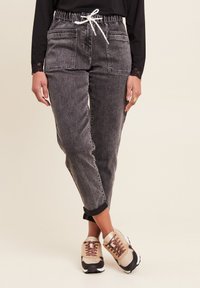 Grijze cargo pants met elastische tailleband, twee voorkoteletten, opgerolde hems en een witte trekkoord, gecombineerd met neutraalgekleurde sneakers.