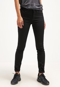 Jean skinny noir avec une texture lisse, taille haute et ourlets retroussés, associés à des chaussures de sport noires. Tissu en mélange de coton.