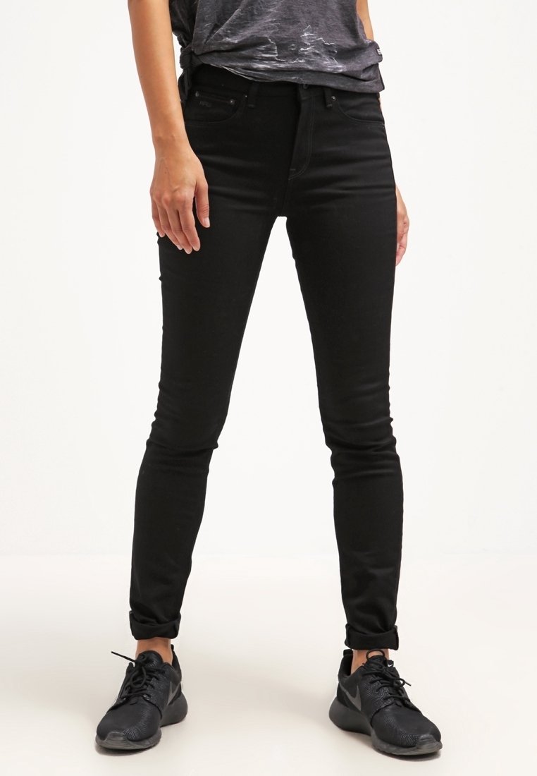 Jean skinny noir avec une texture lisse, taille haute et ourlets retroussés, associés à des chaussures de sport noires. Tissu en mélange de coton.