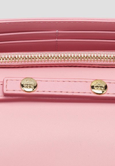 Κοντινή όψη στο εσωτερικό ροζ δερμάτινου πορτοφολιού με χρυστό φερμουάρ και δύο χρυσά κουμπιά σε ραμμένο δερμάτινο λουρί.