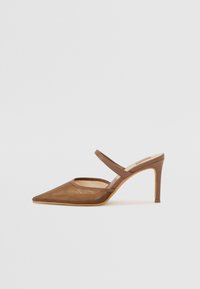 Mules à talons marron avec un bout pointu, des détails en mesh et une fine bride autour de la cheville. Le talon est fin et mesure environ 10 cm.