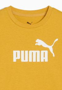 Żółta koszulka z dużym białym logo "PUMA" i sylwetką skaczącej pumy nad napisem, z okrągłym dekoltem.