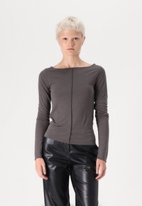 Chemise grise à manches longues avec un col bateau, fabriquée en tissu doux. Présente une couture centrale et un design ajusté, associée à un pantalon en cuir noir.