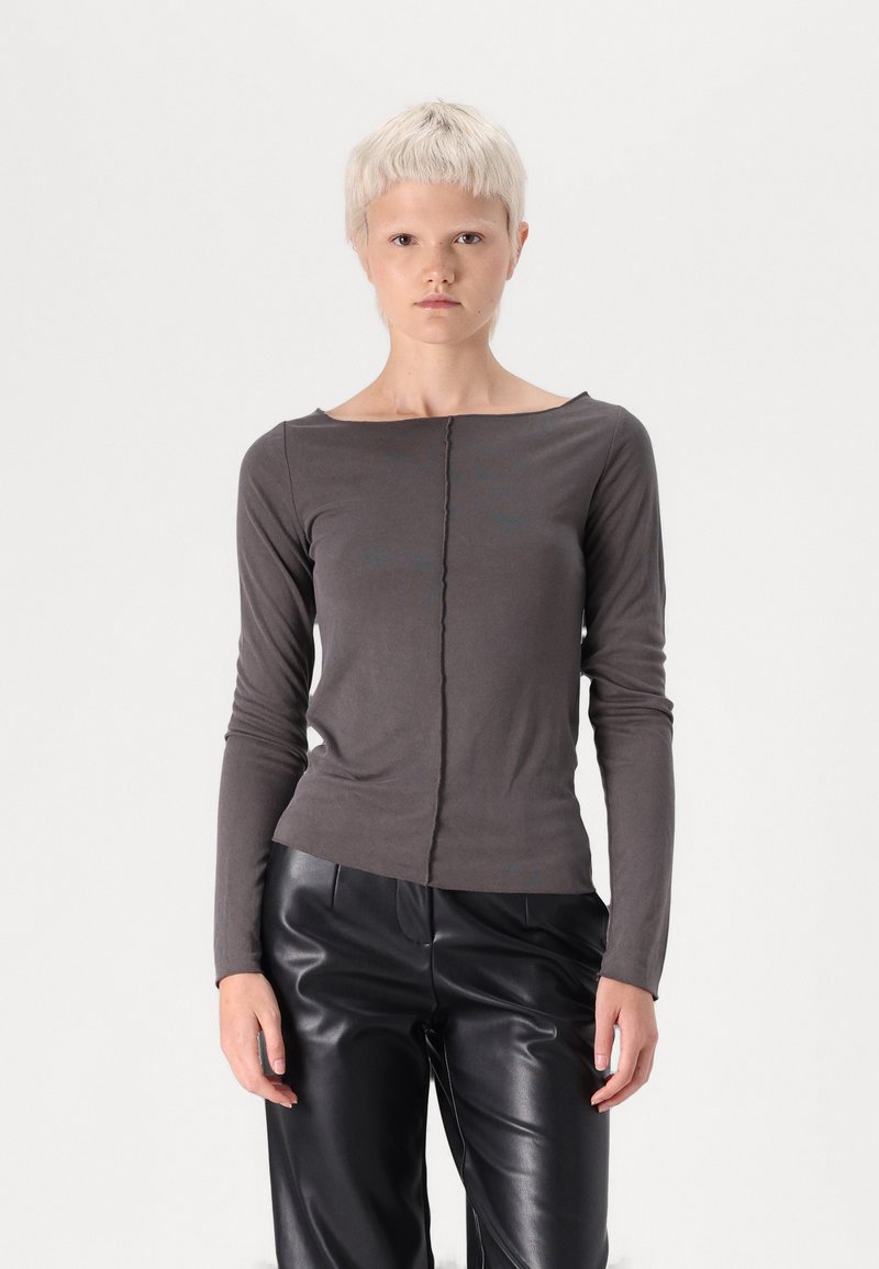 Chemise grise à manches longues avec un col bateau, fabriquée en tissu doux. Présente une couture centrale et un design ajusté, associée à un pantalon en cuir noir.
