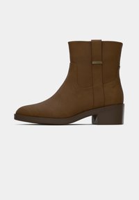 Καφέ μποτάκι αστραγάλου με λεία δερμάτινη επιφάνεια, στρογγυλή μύτη, κοντό τακούνι τύπου μπλοκ και θηλύκι στο πίσω μέρος για εύκολη φόρεση.