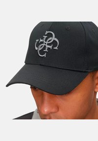Gorra de béisbol negra con visera curva, que presenta un destacado logo bordado en gris en la parte frontal. La tela es suave con un acabado mate.
