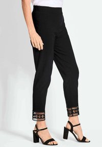 Zwarte broek met een aansluitend ontwerp, textuurzoom met open gebreide geometrische patronen; gecombineerd met zwarte block-heel sandalen.