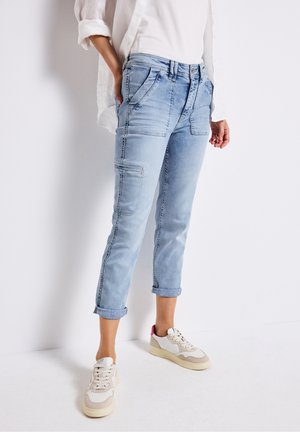 Jeans cargo in denim chiaro con risvolti, tasche frontali piatte e una vestibilità rilassata, abbinati a sneakers di colore crema e rosa.
