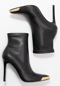 Czarne botki na obcasie z odkrytymi kostkami, z złotymi metalowymi czubkami w kształcie szpica, gładka skóra na cholewce i smukłe obcasy typu stiletto.