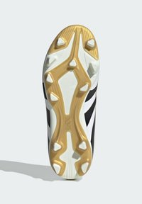 Black and white sports shoe sole featuring a golden section, textured pattern, and multiple molded studs for traction on grass surfaces.