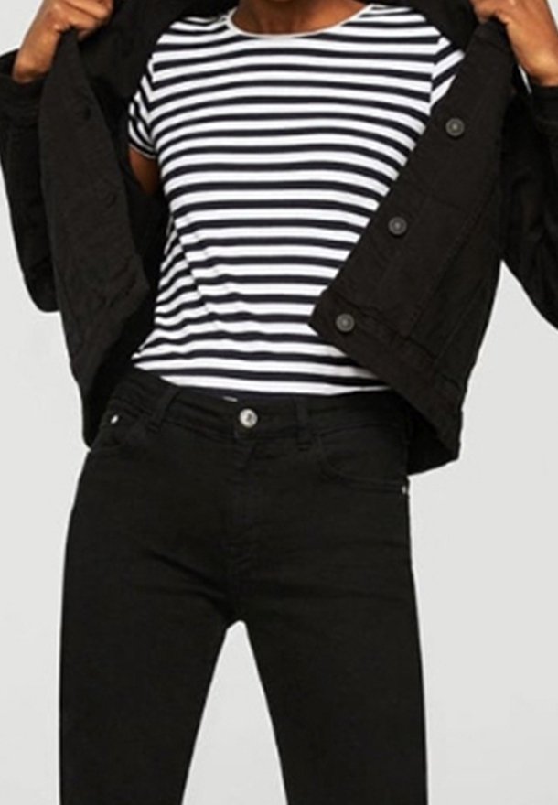 Veste en denim noire portée sur un t-shirt rayé blanc et bleu marine, associée à un jean noir. Détails clés : boutons sur la veste et coupe ajustée.