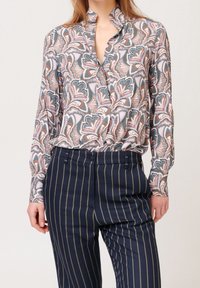 Blouse à manches longues en tissu léger avec un motif cachemire multicolore. Dotée d'un col et d'un ourlet légèrement froncé. Portée avec un pantalon rayé bleu marine.