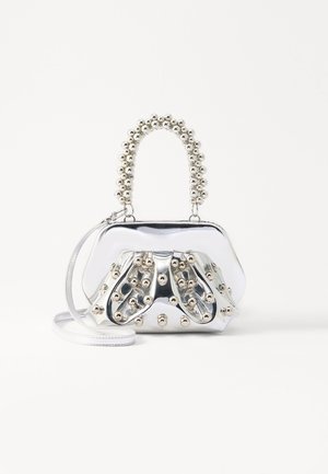 Strieborná metalická kabelka s okrúhlym tvarom, ozdobená guľovitými akcentmi a korálkovou rúčkou. Obsahuje odnímateľný ramenný popruh.