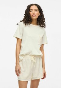 Camiseta de algod�ón color beige claro con mangas cortas y un bolsillo que presenta un diseño de encaje, combinada con pantalones cortos texturizados beige claro con cintura elástica.