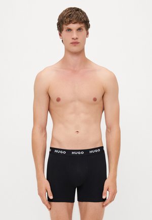 Boxers noirs en coton avec une taille élastique arborant un logo blanc. Le design est ajusté, mettant en avant une texture lisse.