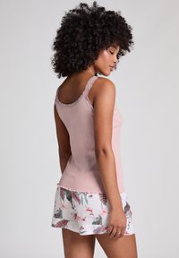 Débardeur rose côtelé avec des bordures en dentelle, associé à un short blanc à motifs floraux avec des accents verts et rouges. Texture lisse, design ajusté.