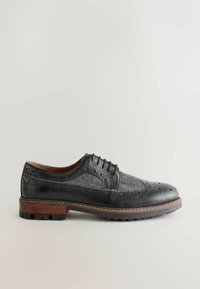 Black leather dress shoe with brogue detailing, patterned texture, lace-up design, and wooden sole, featuring rubber treads for traction.