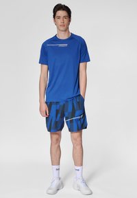 Blå sportt-shirt med korta ärmar och logotyp; matchande blå shorts med geometriskt mönster, fickor och dragkedjedetalj.