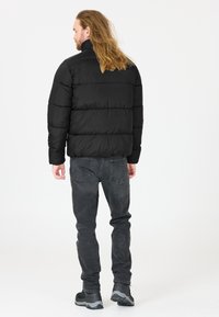 Svart puffjacka med horisontell sömnad, hög krage och en slät yta, ihop med mörkgrå jeans och svarta skor.