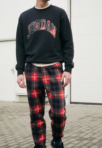 Sudadera oscura con un atrevido estampado de "JORDAN", combinada con pantalones de cuadros en rojo, negro y amarillo, con un corte holgado y cintura elástica.