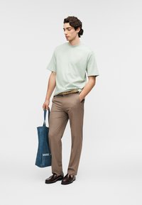 Ανοιχτό πράσινο κοντομάνικο μπλουζάκι, καφέ ραμμένο παντελόνι, σκούρα καφέ παπούτσια και μπλε τσάντα ώμου. Απλές, καθαρές γραμμές και μοντέρνος σχεδιασμός.