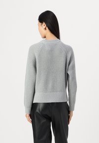 Maglione grigio a maglia con scollatura e orlo a coste. Presenta maniche raglan e una finitura testurizzata. Abbinato a pantaloni neri.