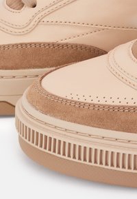 Beige leather sneakers featuring a combination of smooth leather and suede textures, rounded toe, and ridged rubber sole.