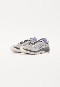 Hellgraue Sneaker mit lila Akzenten, Obermaterial aus Mesh, schwarze Schnürsenkel, runde Zehenpartie, strukturierte Außensohle und seitliche Logodetails.