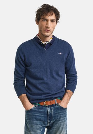 Navyblauwe V-hals trui gemaakt van zacht materiaal, met ribbelmanchetten en -zoom. Gdraagd over een overhemd met kraag en een patroon sjaal. Casual pasvorm.