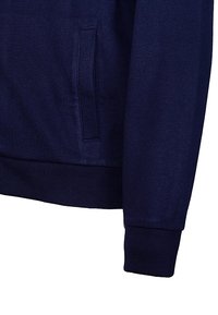 Námornícky modrý sveter vyrobený z látky s hladkou textúrou, s bočnou vreckom a rebrovanými manžetami a spodným lemom pre štruktúrované padnutie.