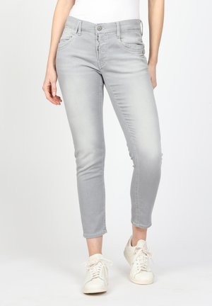 Graue, schmal geschnittene Jeans aus Denim, mit Reißverschluss, fünf Taschen und dezenten Verblassungen, kombiniert mit weißen Sneakern.