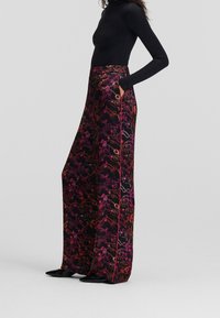 Pantalons larges en tissu noir avec un motif floral vibrant en rose et orange. Comprend des poches latérales et des accents de couture contrastants.