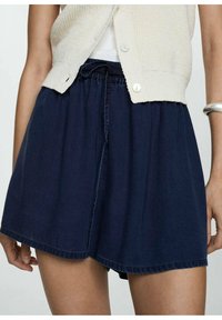 Marineblaue, leichte Shorts mit elastischem Bund, gefälteltem Design und einfarbiger Optik. Kombiniert mit einer cremefarbenen Strickjacke.