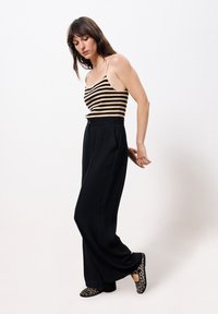 Zwarte wijde broek met hoge taille gecombineerd met een gestreepte beige en zwarte mouwloze top. Schoeisel heeft een luipaardprint ontwerp.