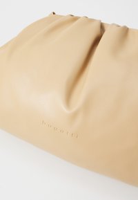 Beige nahkalaukku, jossa on rypytetty muotoilu; siinä on hienovarainen brändinimi "bugatti" painettuna alaosaan. Sileä pinta.