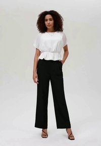 Top peplum branco com mangas curtas, combinado com calças largas pretas de cintura alta. A modelo usa sapatos de salto preto com tiras. Texturas de tecido suaves.