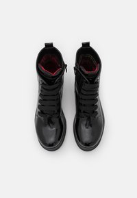 Bottines en cuir verni noir avec détail lacé, présentant une surface texturée et une doublure à carreaux rouges. Fermeture éclair courte sur le côté.