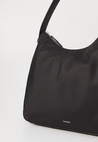 Black nylon handbag with a smooth texture, curved shape, and a single shoulder strap; features a zipper and Calvin Klein branding.