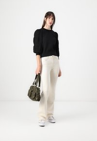 Maglione nero con maniche a palloncino testurizzate, abbinato a jeans chiari a zampa e sneakers bianche. Borsa in tessuto verde con molteplici tasche.