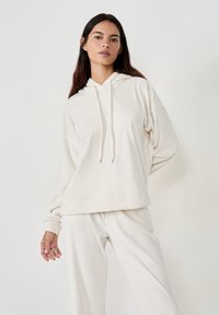 Cremfarbener Kapuzenpullover mit Kordelzug, lässiger Schnitt, langen Ärmeln und passenden cremfarbenen Hosen, aus weichem Material. Minimalistisches Design.