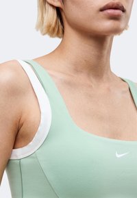 Κοντινό πλάνο ενός ατόμου που φοράει ανοιχτοπράσινο αθλητικό τοπ Nike με λευκές λουρίδες, εμφανίζοντας τον λαιμό, τον ώμο και το πάνω μέρος του στήθους.