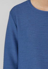 Zils teksturēts apģērbs ar horizontālām ribām, apaļu dekoltē un mīkstu, vieglu audumu. Piemērots ikdienas valkāšanai.