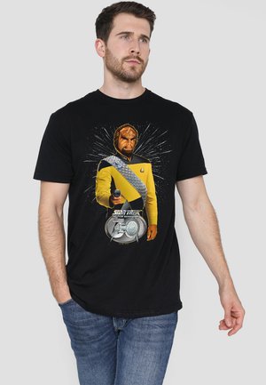 Black t-shirt featuring a graphic of a character in a yellow uniform with silver accents, holding a phaser, against a burst background.