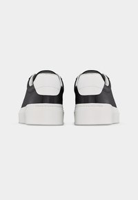 Ζεύγος ασπρόμαυρων αθλητικών παπουτσιών χαμηλού προφίλ με παχιά λευκή σόλα, απεικονιζόμενα από πίσω σε απλό ανοιχτό γκρι φόντο.