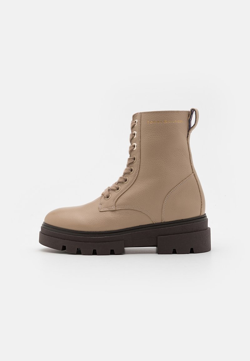 Botte de combat en cuir beige à lacets avec une semelle épaisse à crampons brun foncé et une languette à l’arrière.